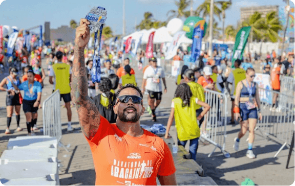 Atleta da Maratona de Aracaju 2025 segura sua medalha em meio à estrutura de chegada.