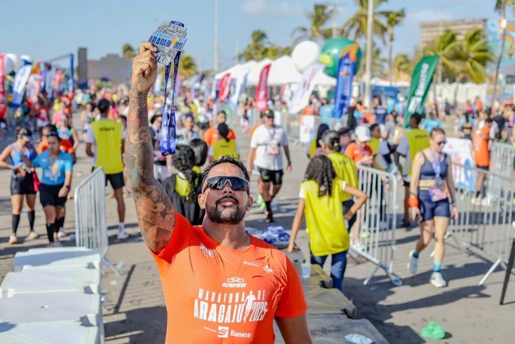 Atleta da Maratona de Aracaju 2025 segura sua medalha em meio à estrutura de chegada.